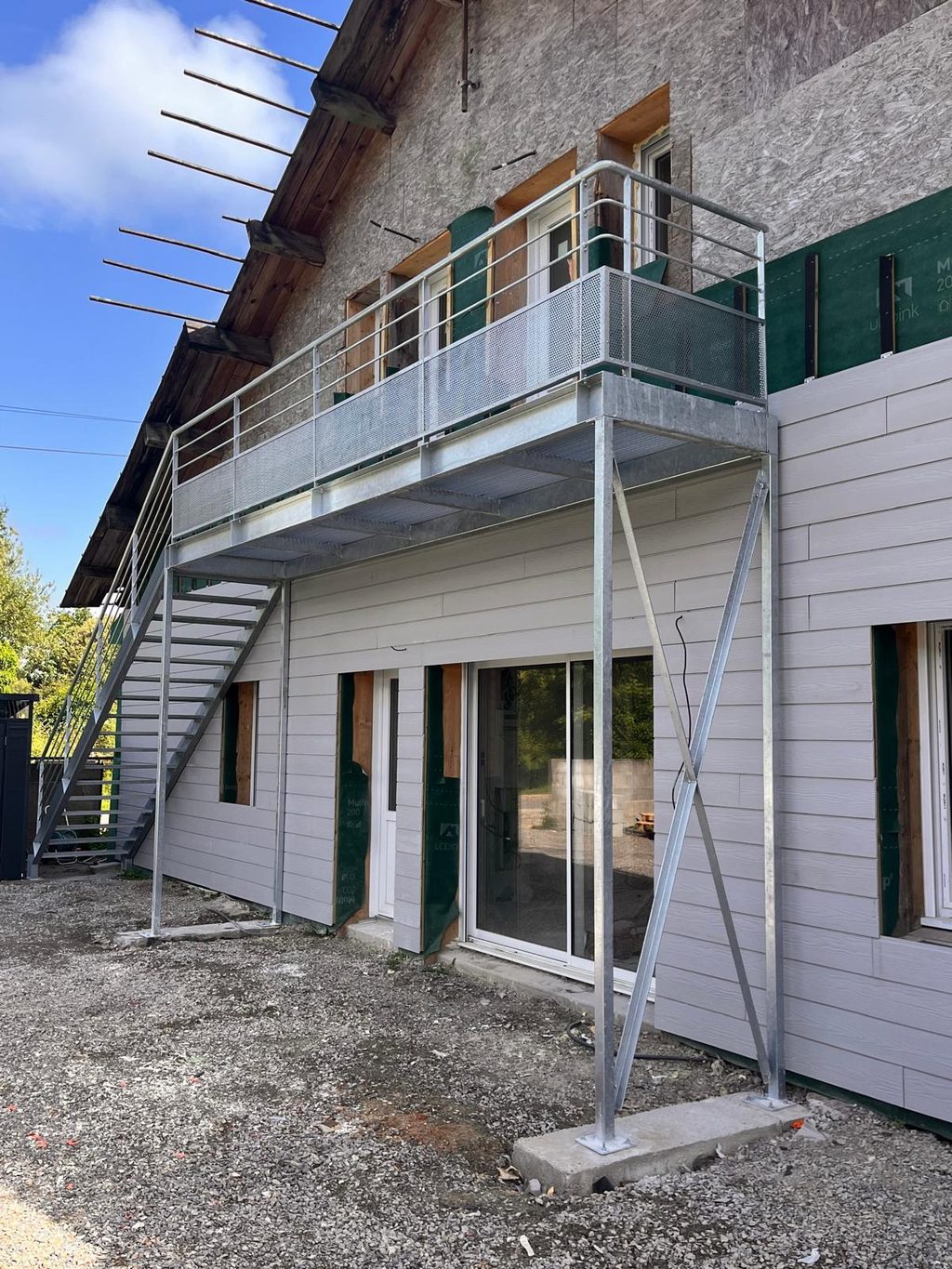 Escalier et balcon extérieurs en acier galvanisé, sur la façade d’une maison.