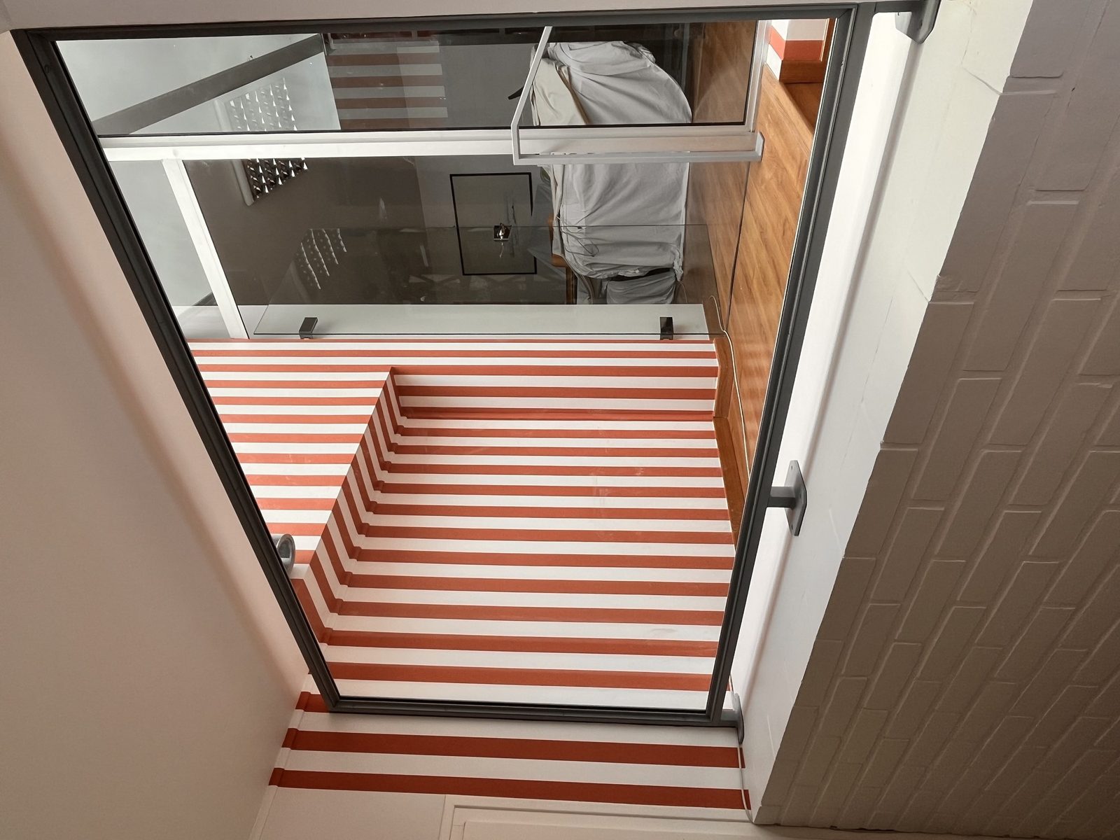Garde-corps vitré à montants fins bordant une cage d’escalier, vu de haut.