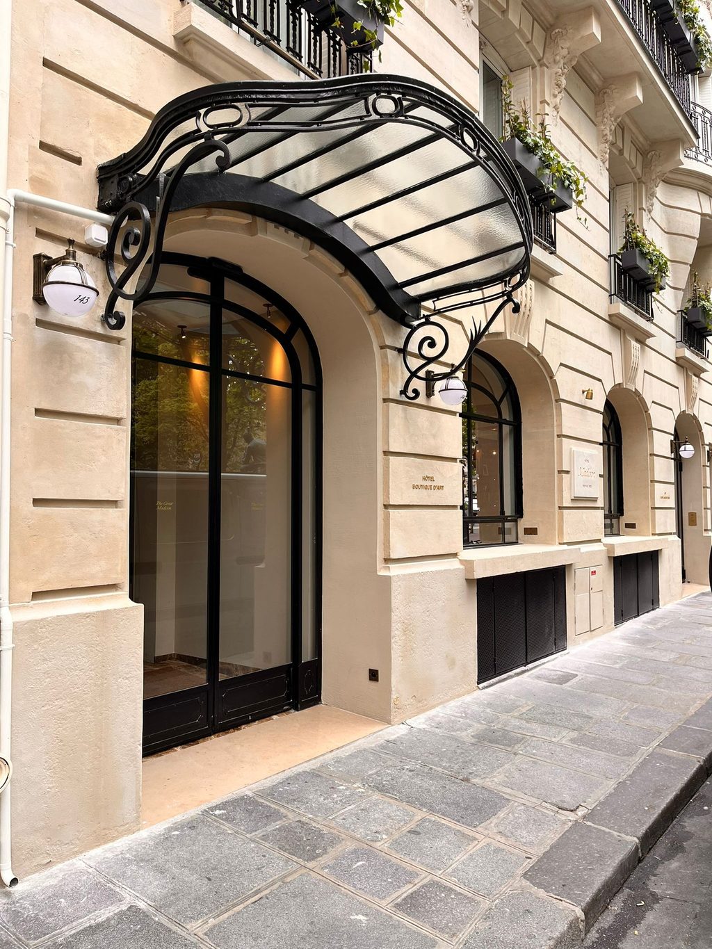 Marquise en fer forgé et verre au-dessus de l’entrée d’un immeuble en pierre de taille.