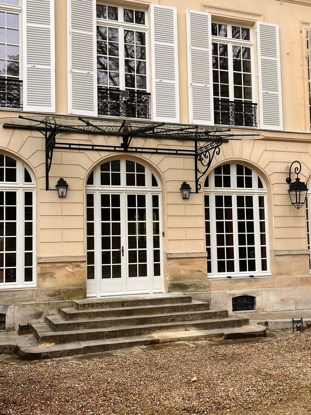 Marquise en fer forgé posée au-dessus de la porte-fenêtre d’une demeure en pierre.