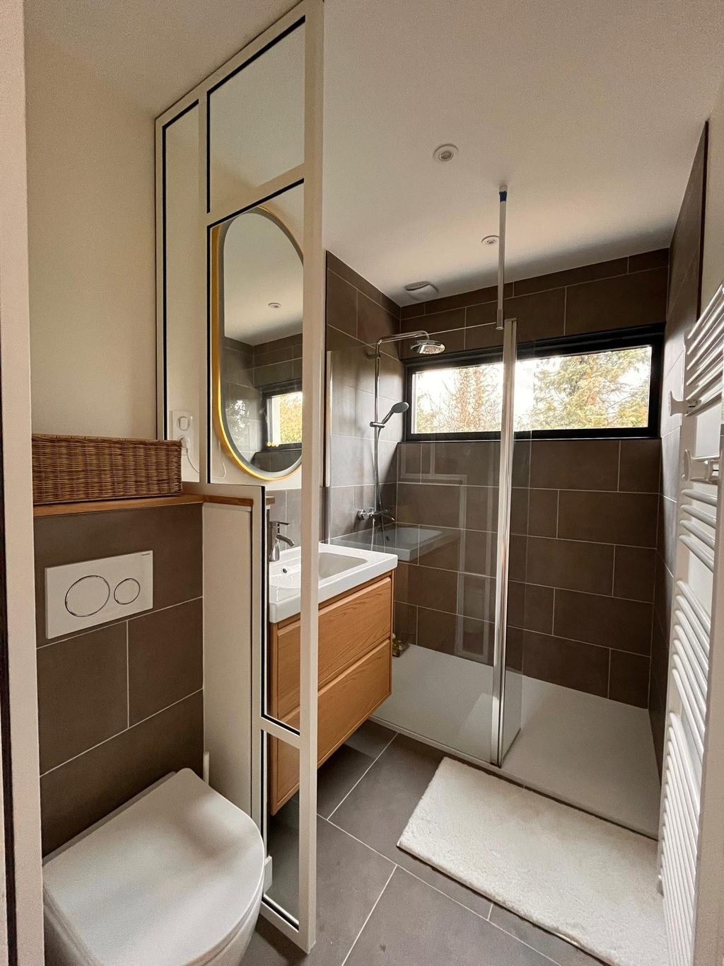 Paroi de douche à cadre d’acier noir et miroir ovale dans une salle d’eau.