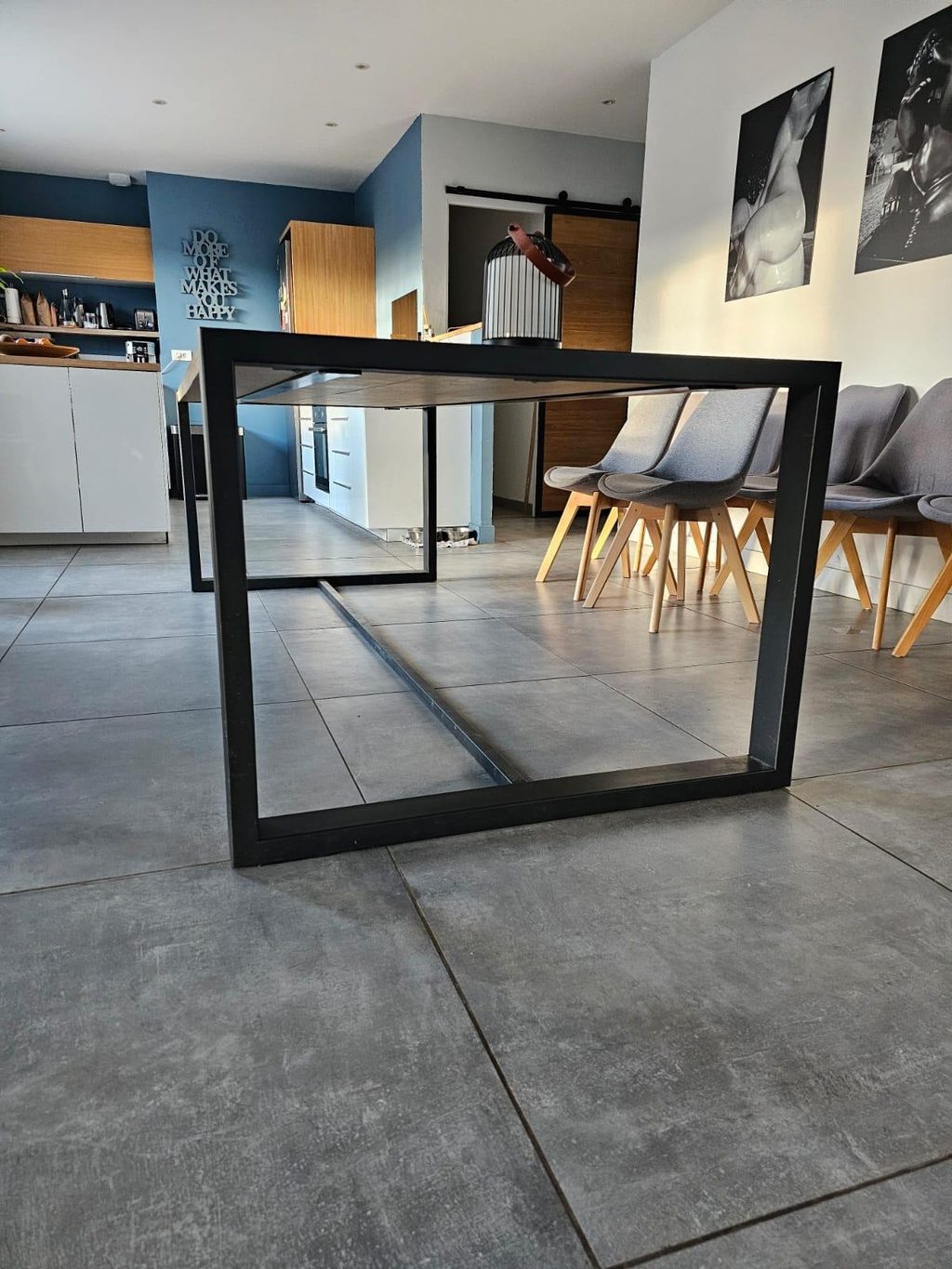 Piètement de table en acier noir posé sur un sol béton, dans une cuisine ouverte.