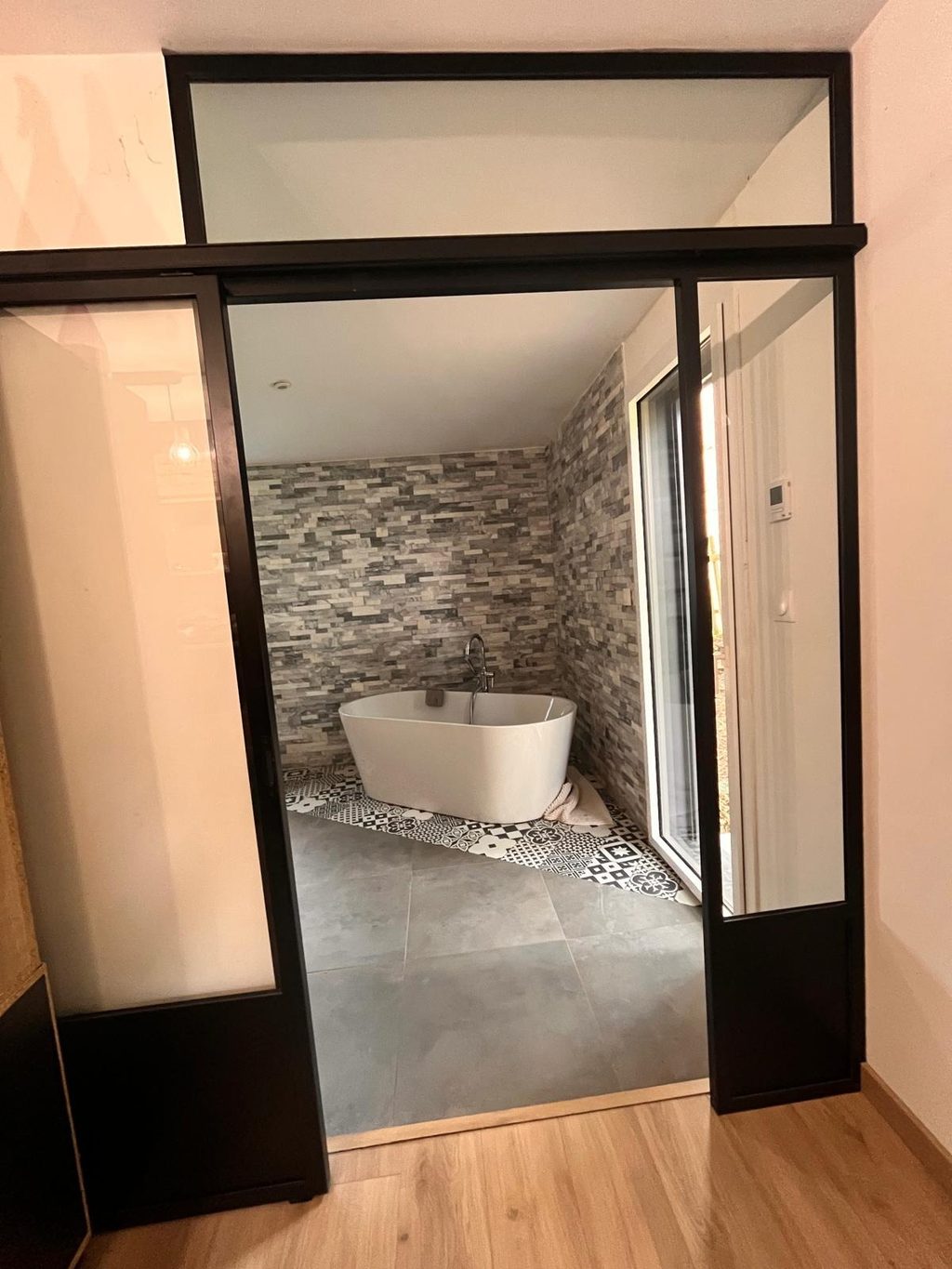Porte vitrée en acier noir ouvrant sur une salle de bains à mur de pierre.