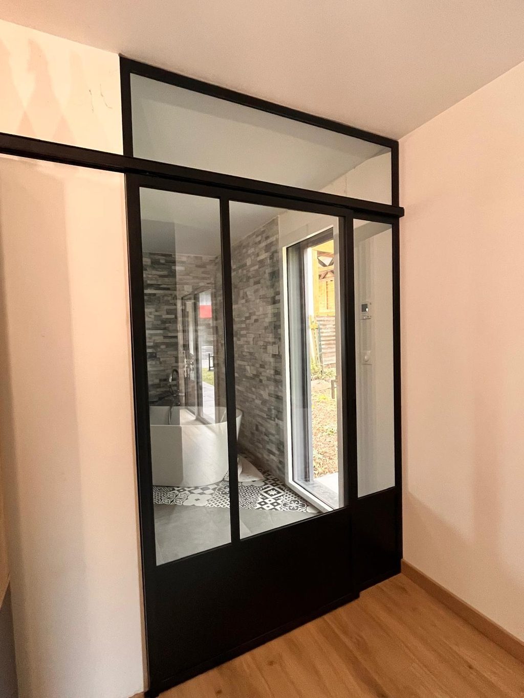 Porte coulissante en acier noir ouvrant sur une salle de bains carrelée.
