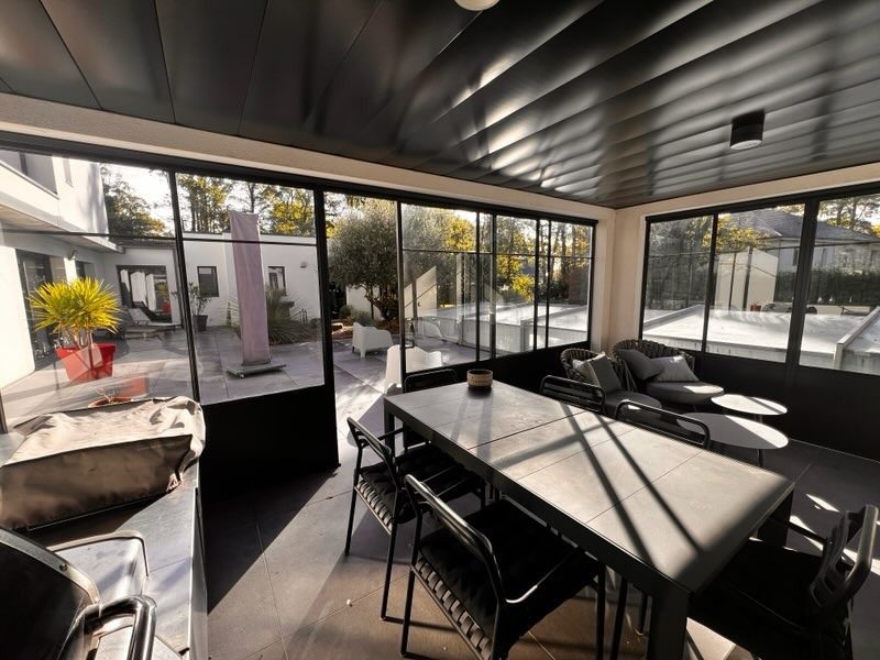Longue table dans une salle vitrée ceinte de menuiseries d’acier noir.
