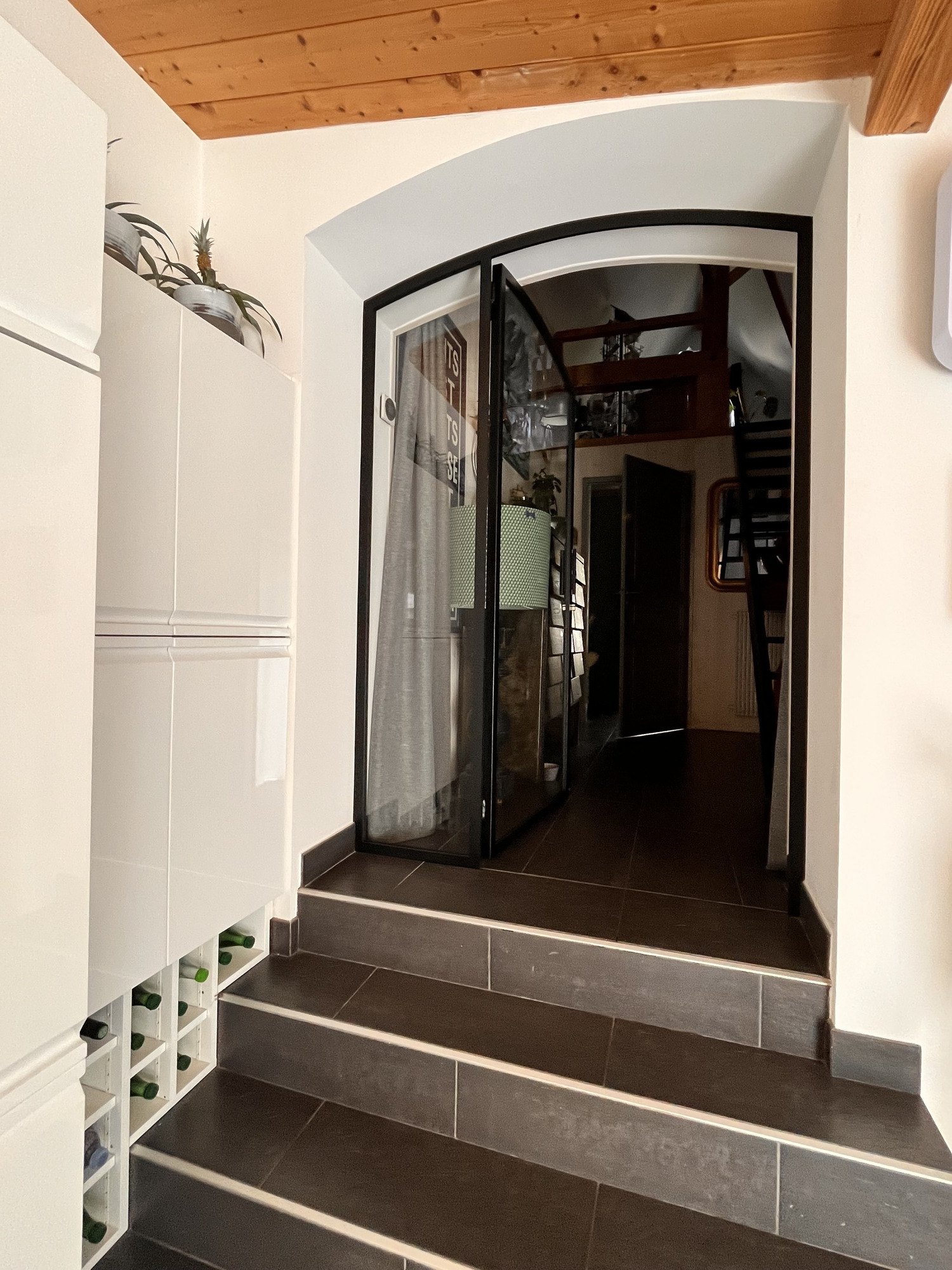 Verrière cintrée à double porte en acier noir, en haut d’un escalier carrelé.