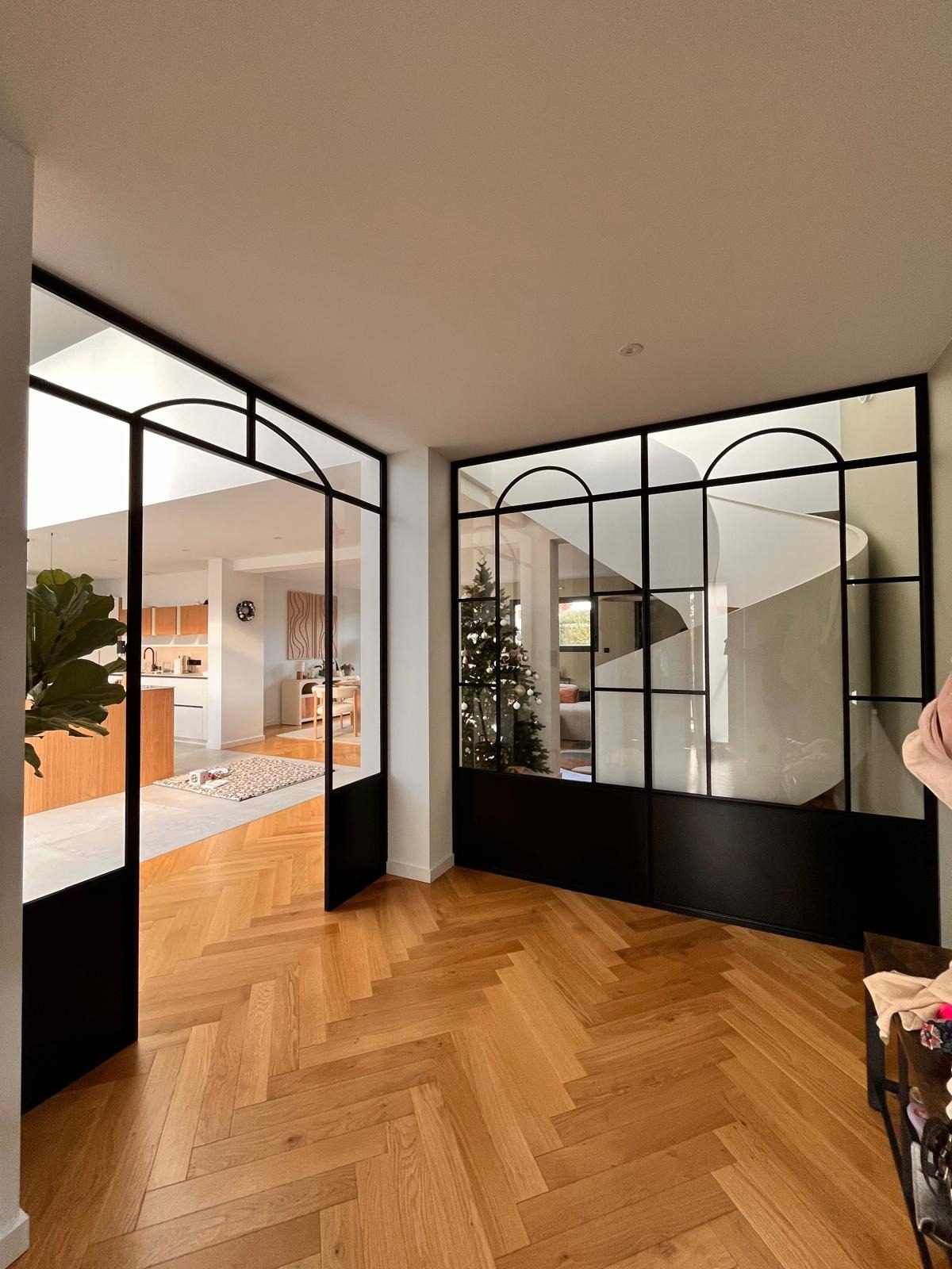 Verrière d’entrée en acier noir à impostes cintrées, sur un parquet à chevrons.