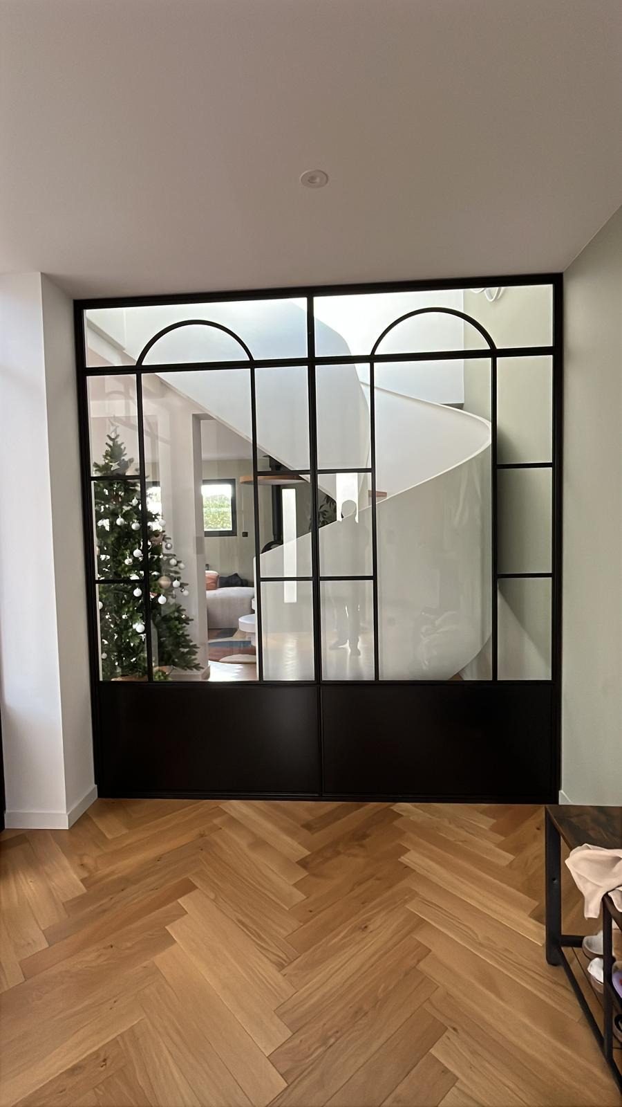 Verrière fixe en acier noir à imposte cintrée, ouvrant sur une entrée.
