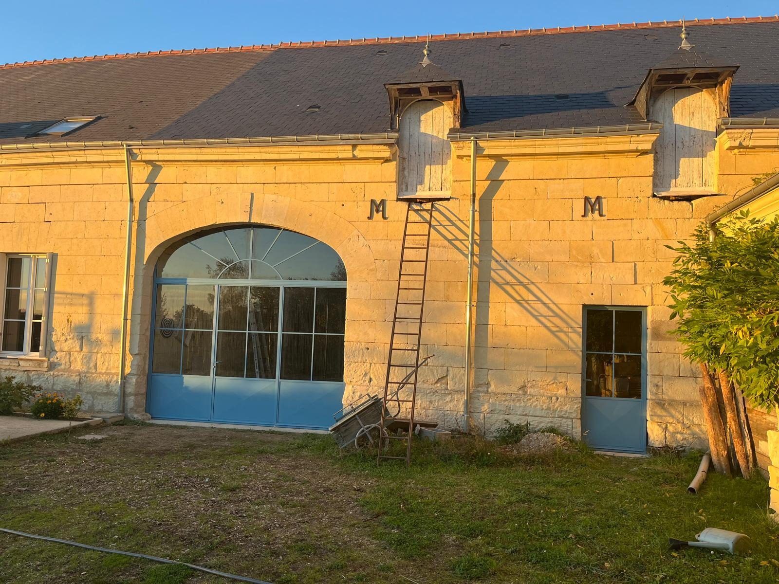 Verrière en acier fermant une arche de pierre, sur la façade d’une longère.