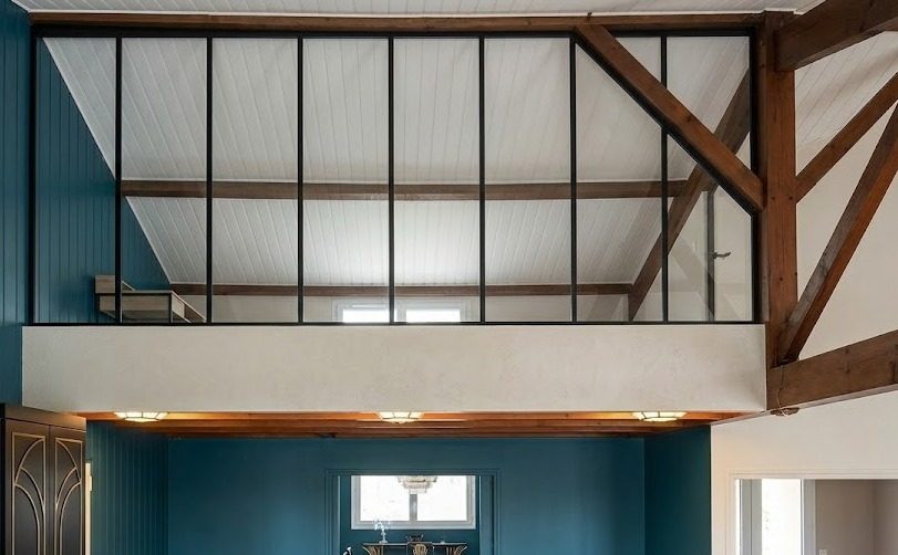 Verrière posée sur un muret de mezzanine, sous une charpente apparente.