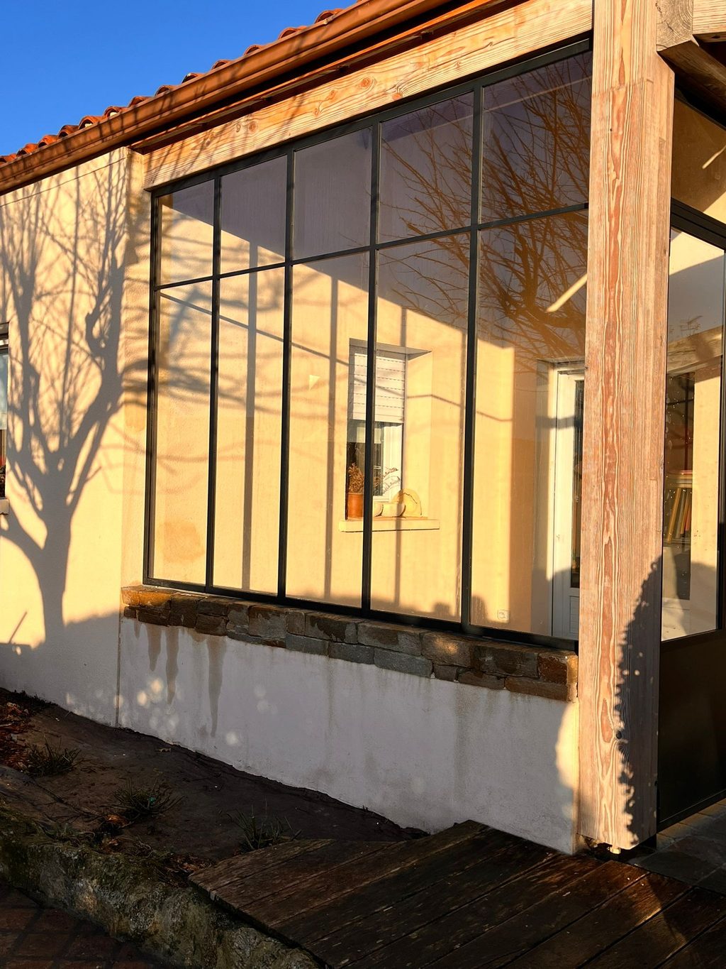 Verrière en acier posée sur un muret, fermant un passage couvert sous charpente.